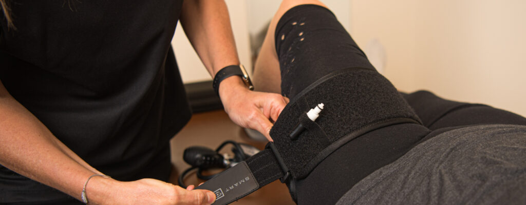 Patient receives blood flow restriction treatment on upper left thigh using a cuff.